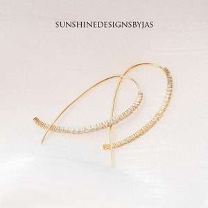 May include: A pair of gold hoop earrings with a row of clear cubic zirconia stones around the edge of each hoop.