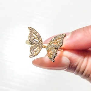 May include: A gold ring with two butterfly designs set with clear cubic zirconia stones.