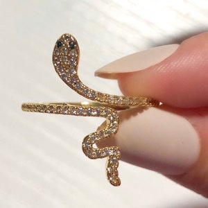May include: A gold snake ring with clear cubic zirconia stones. The snake is coiled and the head is facing forward.