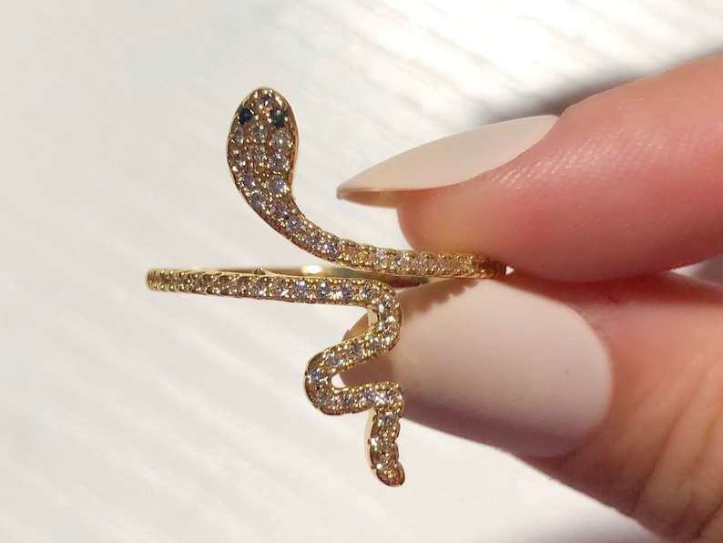 May include: A gold snake ring with clear cubic zirconia stones. The snake is coiled and the head is facing forward.