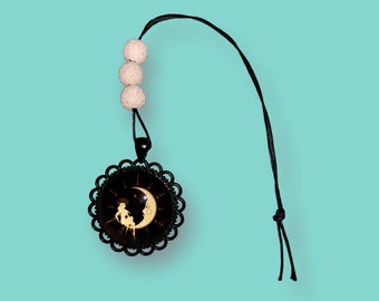 May include: A black necklace with a round pendant featuring a moon and stars design. The pendant is surrounded by a black filigree frame. The necklace has three white beads.