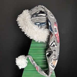May include: A long, gray fleece stocking cap featuring a repeating pattern of various beverage bottles and glasses. The hat is trimmed with a thick, white, curly faux fur cuff and finished with a matching white pom-pom at the pointed tip.
