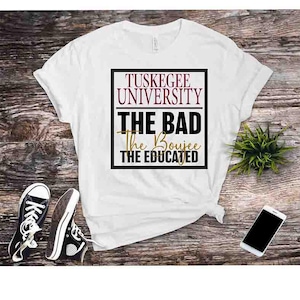 May include: White t-shirt with the text "Tuskegee University" above "The Bad, The Boujee, The Educated" in a black and maroon design. Black and white sneakers and a smartphone are also visible.