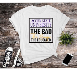 May include: White t-shirt with the text "ACORN STATE UNIVERSITY" in purple and black. Below the university name, the shirt reads "THE BAD, The Boujee, THE EDUCATED" in black and gold. Black sneakers and a smartphone are also visible.
