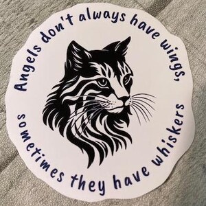May include: Black and white sticker with a cat's head and the text "Angels don't always have wings, sometimes they have whiskers."