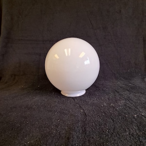 May include: A white glass globe light fixture with a smooth, shiny finish. The globe is round and sits on a small, flat base.
