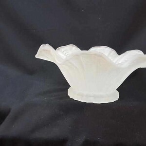 May include: A white frosted glass bowl with a ruffled edge. The bowl is shaped like a flower and has a smooth, rounded bottom.