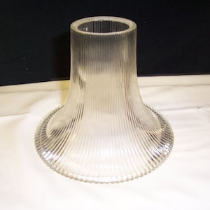 May include: A clear glass lampshade with a ribbed design. The shade is bell-shaped and has a wide, flared base.
