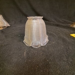 Puede incluir: Una pantalla de lámpara de vidrio transparente con un diseño texturizado y acanalado. La pantalla tiene un borde festoneado y una forma de campana.