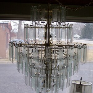 May include: A large, multi-tiered chandelier with clear glass panels and a gold metal frame. The chandelier is hanging from a chain.