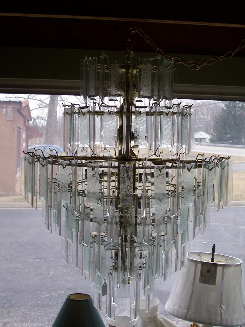 May include: A large, multi-tiered chandelier with clear glass panels and a gold metal frame. The chandelier is hanging from a chain.