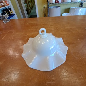 Puede incluir: Pantalla de lámpara de porcelana blanca con borde rizado y asa de anillo. La pantalla de la lámpara está sobre una mesa de madera.