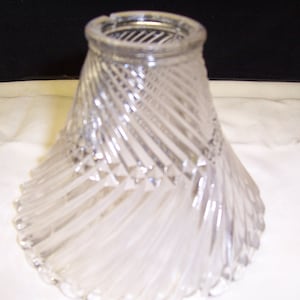 May include: A clear glass lampshade with a spiral design. The shade has a wide, flared bottom and a narrow top.