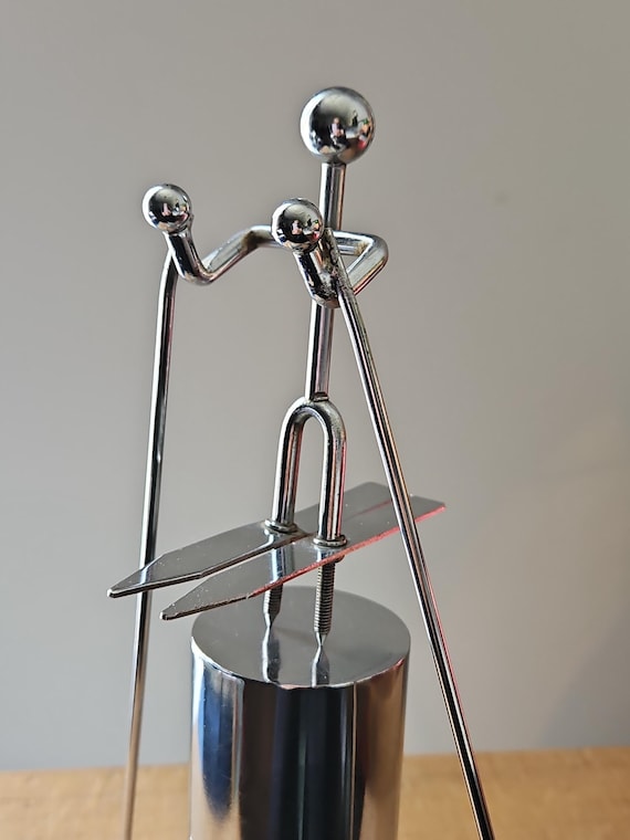 A hand-balanced metal figure skier that rocks and pivots with satisfying kinetic motion — the kind of desk toy you'd find in a cool architect's office.