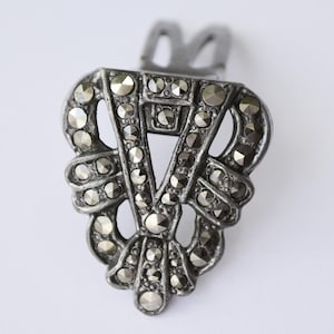 May include: A dark grey metal hair clip featuring a triangular openwork design adorned with numerous small, faceted, dark grey stones. The accessory has a symmetrical, geometric pattern with a clip mechanism visible at the top section.