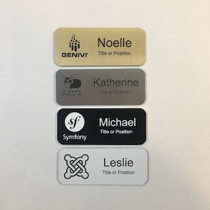 May include: Four different name tags with company logos and names. The top tag is gold with a black logo and the name "Noelle" with the title "Title or Position". The second tag is silver with a black sheep logo and the name "Katherine" with the title "Title or Position". The third tag is black with a white logo and the name "Michael" with the title "Title or Position". The bottom tag is white with a black logo and the name "Leslie" with the title "Title or Position".