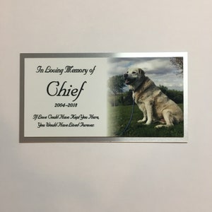 May include: A memorial plaque with a silver border. The left side has text that reads "In Loving Memory of Chief 2004-2018" and a quote. The right side features a photo of a light-colored dog sitting on grass.