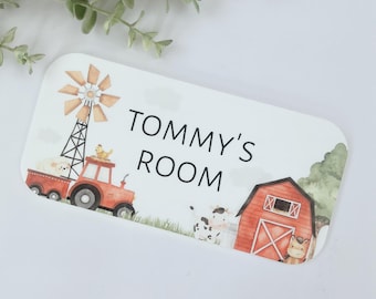 Könnte beinhalten: Ein weißes Türschild mit einem roten Stall, einem Traktor, einer Windmühle und einer Kuh. Das Schild trägt die Aufschrift "Tommy's Room" in schwarzer Schrift.
