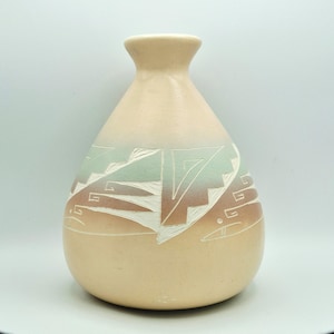 May include: A beige ceramic vase with a rounded body and a narrow neck. The vase features a geometric design in shades of white, green, and brown. The design is etched into the surface of the vase. The vase is a decorative item.