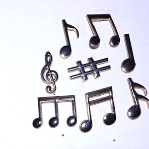 May include: A collection of silver-colored musical notes and symbols, including eighth notes, quarter notes, and a treble clef, arranged on a white surface. The metallic objects have a reflective quality.