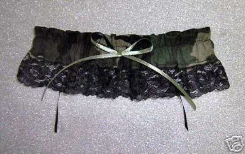 Puede incluir: Una liga de camuflaje verde y negro con un lazo de sat&eacute;n blanco y ribete de encaje negro.