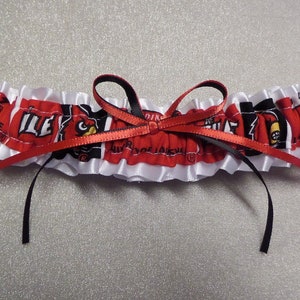 May include: White satin garter with a red and black ribbon bow. The garter features a red and black fabric with a repeated pattern of a cardinal bird and the word "Louisville".
