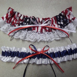 May include: Two bridal garters, one with a red, white, and blue American flag print and white lace trim, and the other with white satin and navy blue satin stripes.
