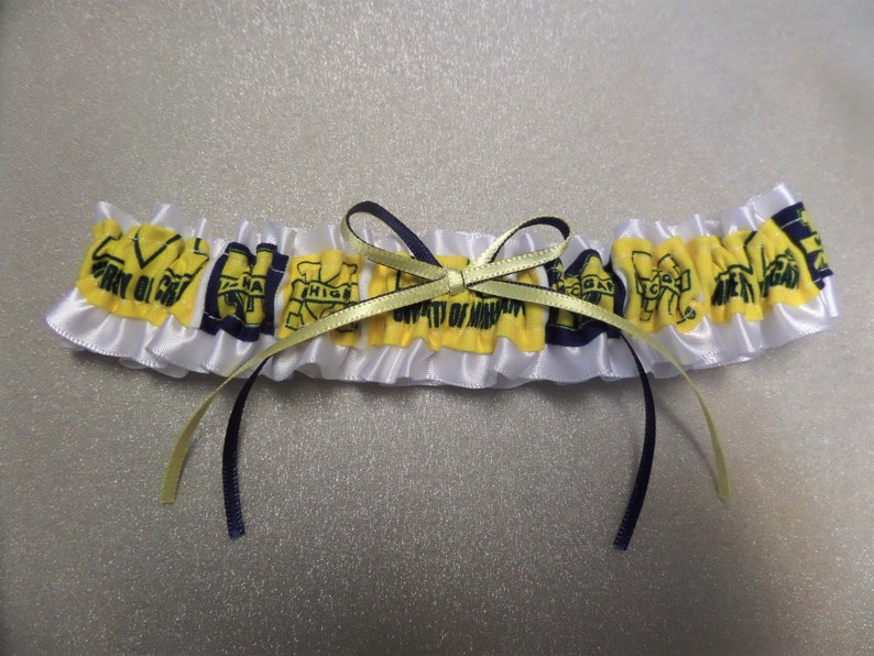 May include: White satin garter with yellow and blue fabric accents. The fabric accents feature the University of Michigan logo and the text "University of Michigan".