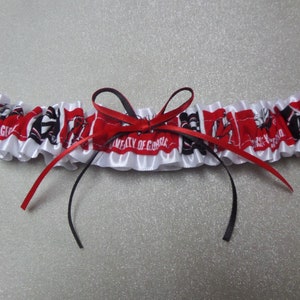May include: White satin garter with red and black ribbon bow. The garter has a red and white fabric with the text "University of Georgia" and a black and white logo.