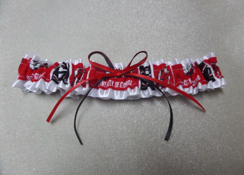 May include: White satin garter with red and black ribbon bow. The garter has a red and white fabric with the text "University of Georgia" and a black and white logo.