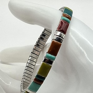 Könnte beinhalten: Ein elastisches Armband mit rechteckigen Segmenten aus poliertem Stein in Türkis, Olivgrün, Braun und Dunkelrot, die durch dünne silberfarbene Metallabstandshalter getrennt sind. Das Band besteht aus einem flexiblen, dehnbaren Metallgliederdesign.