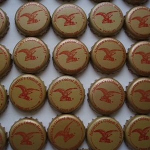 May include: A collection of gold bottle caps with the text "America's Oldest Brewery" and a red eagle design.