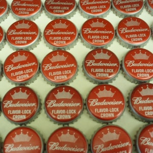 May include: A collection of red and silver bottle caps with the Budweiser logo and the text "Flavor-Lock Crown".