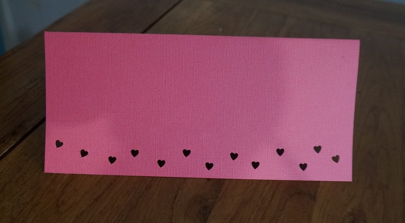 Puede incluir: Una tarjeta rosa con una fila de corazones negros a lo largo del borde inferior.