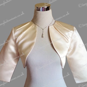 May include: A short-sleeved, ivory satin bolero with a draped neckline. The bolero is on a white mannequin.