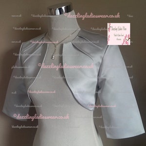 May include: A silver satin bolero with three-quarter sleeves. The bolero has a draped neckline and a fitted silhouette.