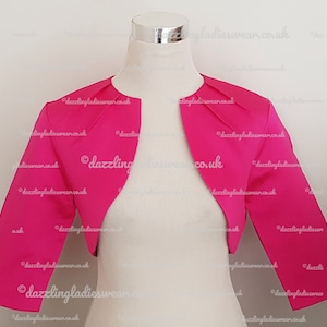 Puede incluir: Un bolero rosa intenso con mangas tres cuartos. El bolero está hecho de una tela lisa y sedosa.