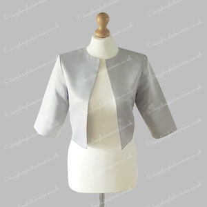 May include: A silver satin bolero jacket with three-quarter sleeves. The jacket has a V-neckline and is open in the front.