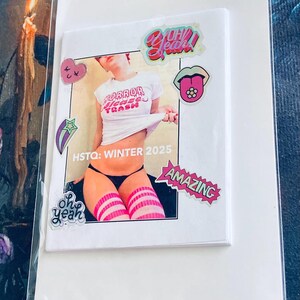 May include: A white t-shirt with the text "Mirror Mirror On The Trash" and a pink heart sticker, a pink tongue sticker, a pink star sticker, a pink "Oh Yeah!" sticker, and a pink "Amazing" sticker. The text "HSTQ: Winter 2025" is printed below the t-shirt.