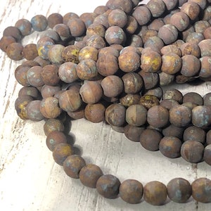 May include: Strands of round, matte beads in shades of brown, with hints of blue and yellow. The beads have a rustic, weathered appearance, suggesting a natural or vintage aesthetic. Ideal for jewelry making or craft projects.