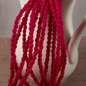 May include: Strands of bright pink beads cascade from a white ceramic pitcher. The beads have a faceted, geometric shape, creating a textured appearance. The image highlights the contrast between the smooth pitcher and the beaded strands.