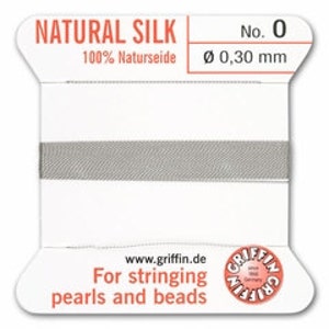 May include: A spool of natural silk thread, labeled "NATURAL SILK" and "No. 0". The label indicates the thread is 100% Naturseide with a diameter of 0.30 mm. Text on the label reads "For stringing pearls and beads". The spool is white with gray thread.
