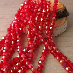 May include: Strands of faceted, bright red beads. The beads have a sparkling, iridescent quality, catching the light. The beads are strung together, creating a flowing, textured appearance. The beads are likely for jewelry making or crafting.