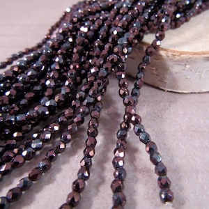 May include: Strands of small, faceted beads in shades of dark purple and bronze. The beads have a metallic sheen and are strung together, creating a textured and shimmering effect. Ideal for jewelry making.