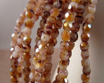 May include: Strands of faceted beads in shades of brown, cream, and amber. The beads have a marbled appearance and a reflective, iridescent quality. The beads are strung together, creating a cascading effect. The beads are likely for jewelry making.