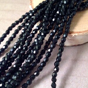 May include: Strands of faceted black beads. The beads have a glossy finish and are strung together, creating a textured and reflective surface. The beads are likely used for jewelry making or crafting.