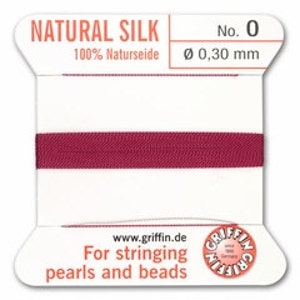 May include: A spool of natural silk thread, labeled "NATURAL SILK" and "No. 0." The thread is a deep burgundy color, and the spool has text that reads "100% Naturseide" and "Ø 0,30 mm." The packaging also includes the website "www.griffin.de" and the text "For stringing pearls and beads."