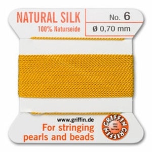 May include: A spool of yellow natural silk thread, labeled "NATURAL SILK No. 6" with a diameter of 0.70 mm. The label also includes the text "For stringing pearls and beads" and the website www.griffin.de.