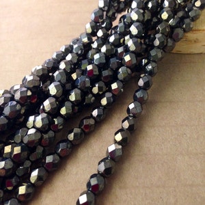 May include: Strands of faceted, dark gray beads. The beads have a metallic sheen and are strung together, creating a textured and reflective surface. The beads are arranged in a diagonal pattern, showcasing their individual shapes and the overall design.