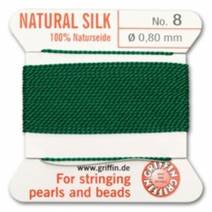 May include: A spool of dark green natural silk thread, labeled "NATURAL SILK No. 8" with "100% Naturseide" and "Ø 0,80 mm" printed on the label. The label also includes "For stringing pearls and beads" and the website address.